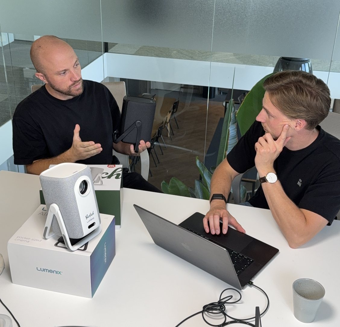 Dion en Maarten van Lumenix aan tafel op kantoor, met een Lumenix-beamer en een laptop