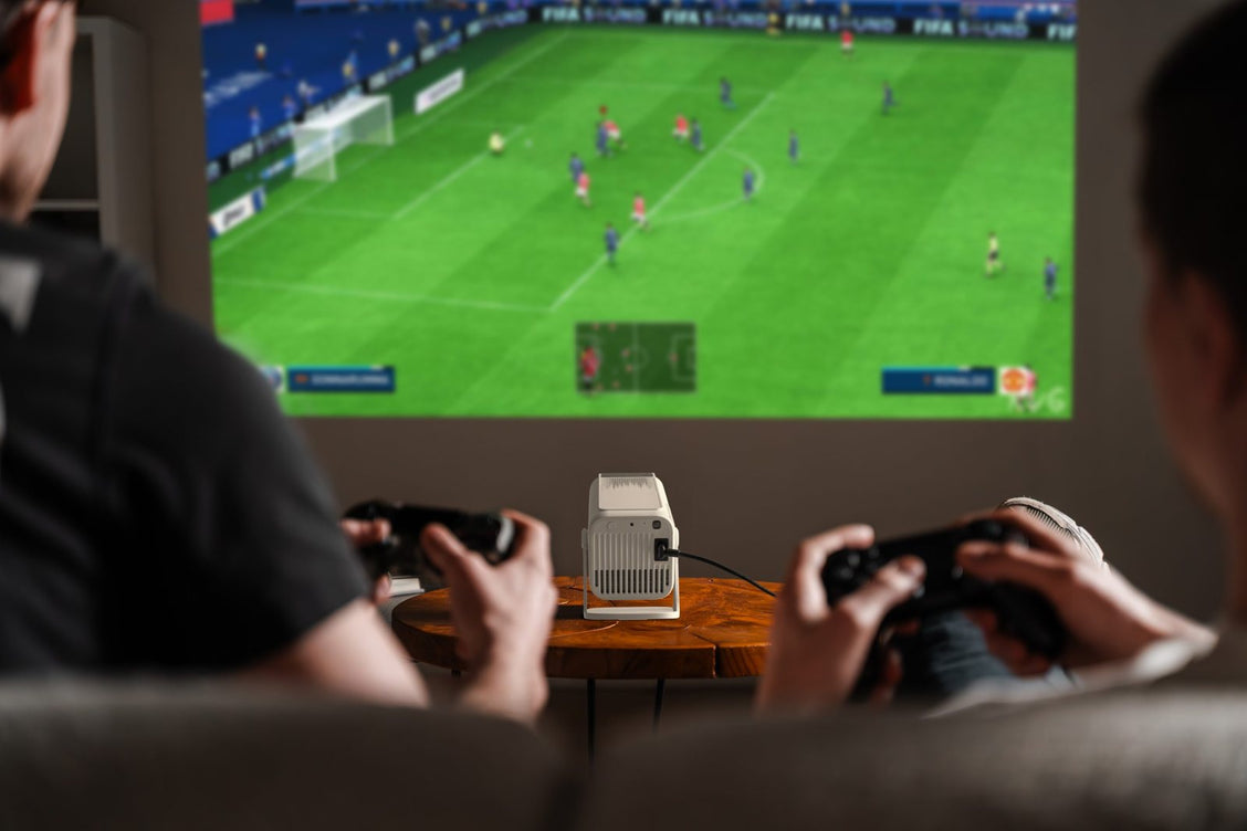 Twee mensen gamen op de bank met een Lumenix die een voetbalgame groot op de muur projecteert