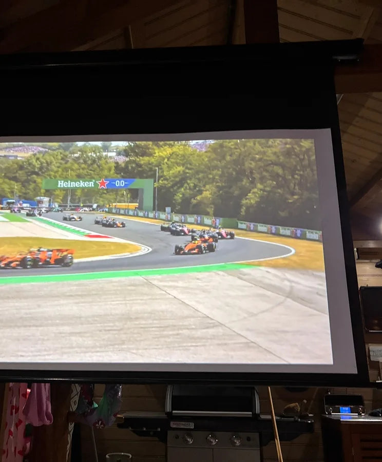 Foto van Gilbert: een autorace op een oprolscherm, in een ruimte met houten wanden
